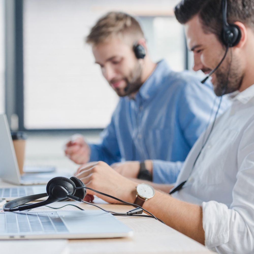 smiling-young-call-center-operators-in-headsets-using-laptops-in-office-1